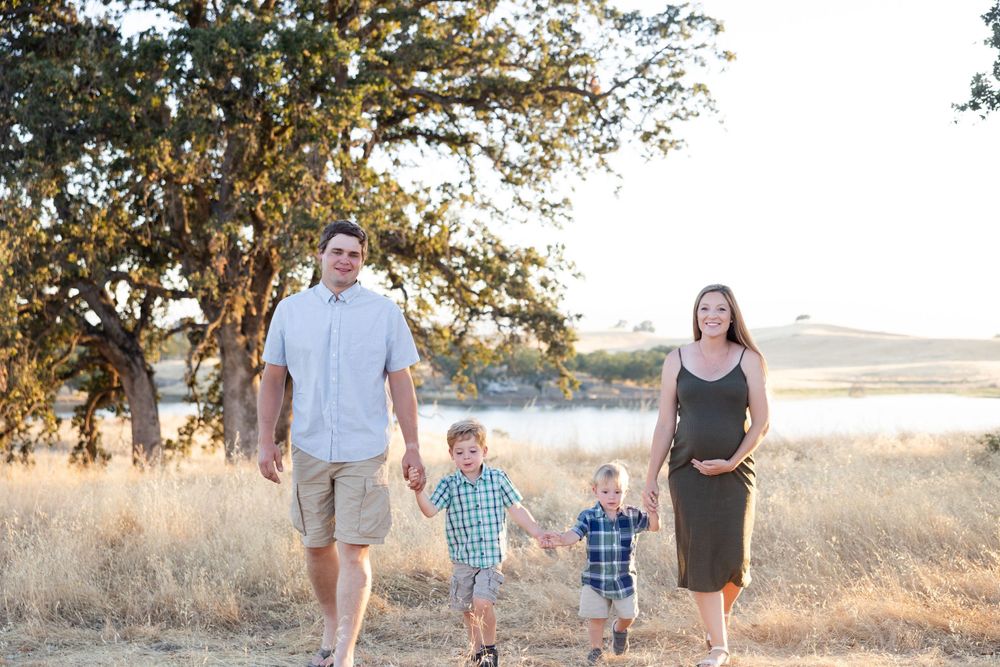 Family of four walking together through golden field at sunset.