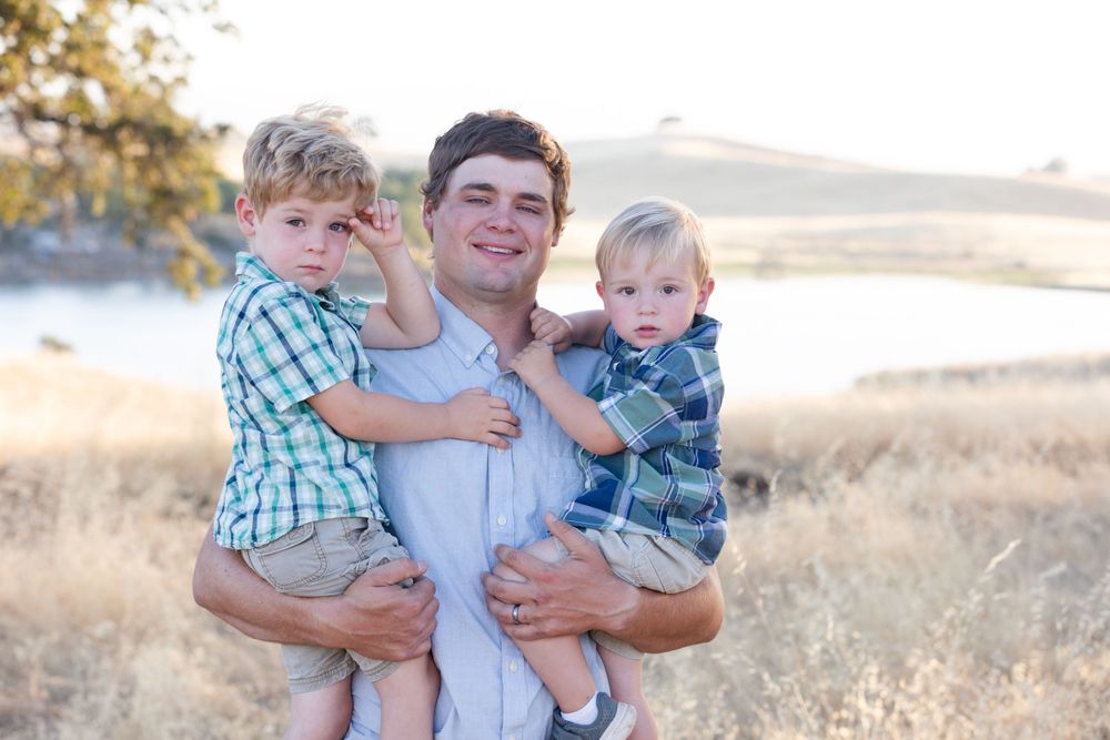 A loving outdoor family portrait captured in golden sunlight with rolling hills in the background during sunset.