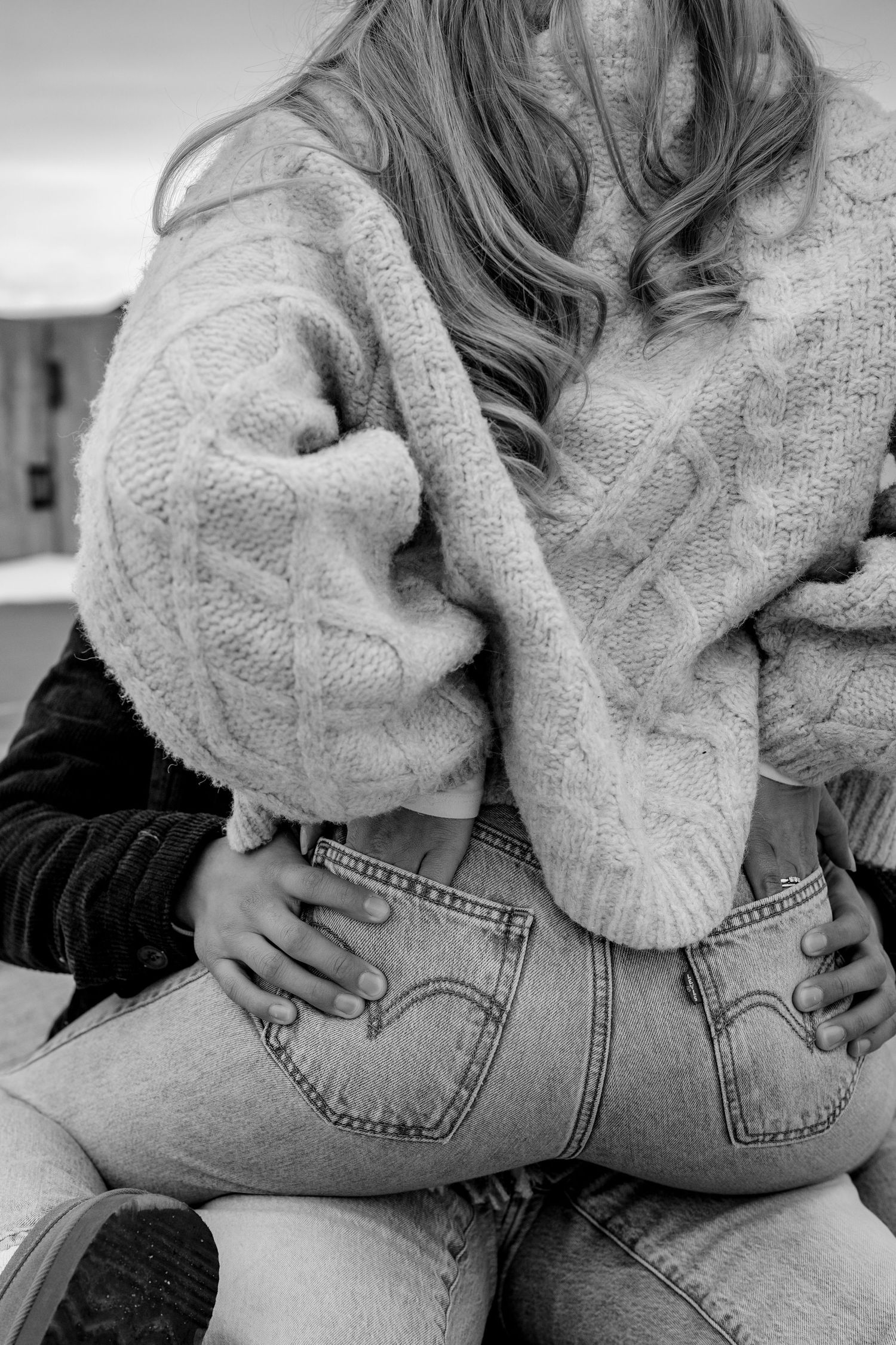 A couple in casual wear embraces intimately, wearing a cozy sweater and denim jeans in black and white.