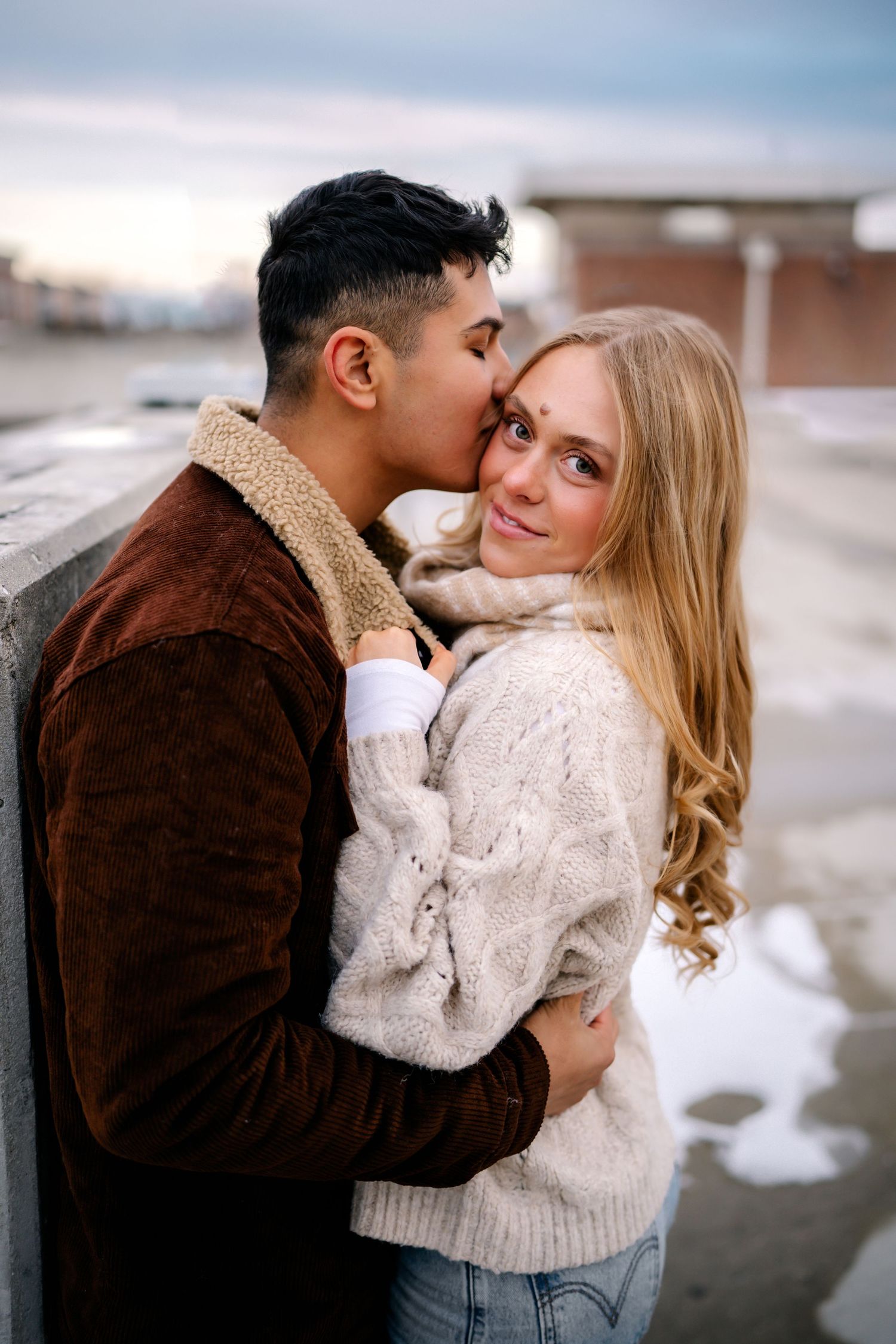 Two people in winter sweaters share an intimate embrace outdoors on a cold winter day.