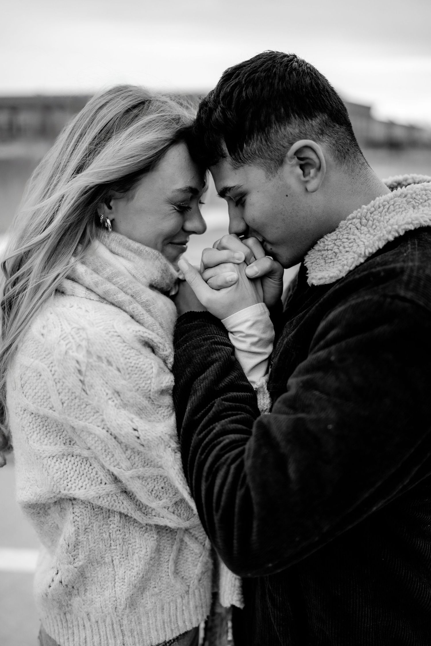 A romantic black and white portrait of a couple in cozy winter sweaters touching foreheads in an intimate moment.