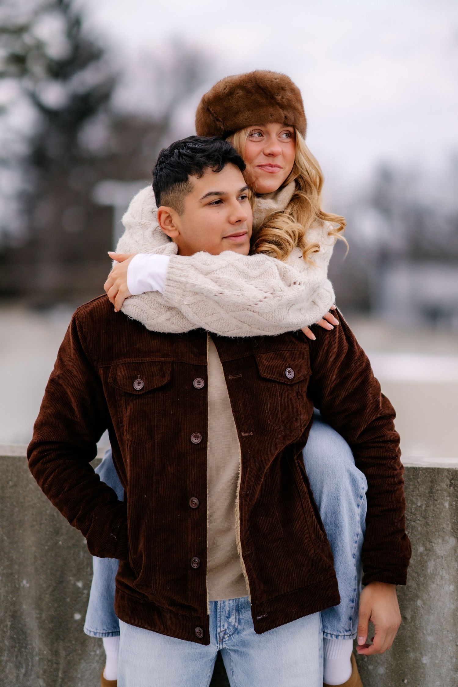 A couple in warm winter clothing share a tender moment outdoors on an overcast day.