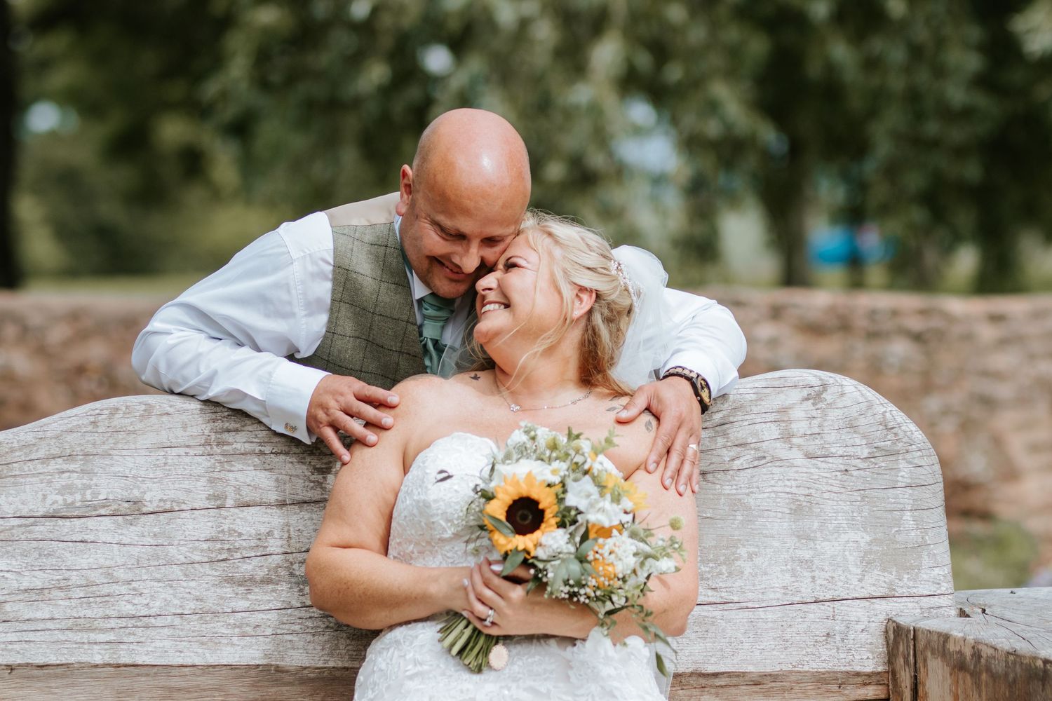 A romantic wedding moment on a rustic wooden bench with a bridal bouquet featuring bright sunflowers.