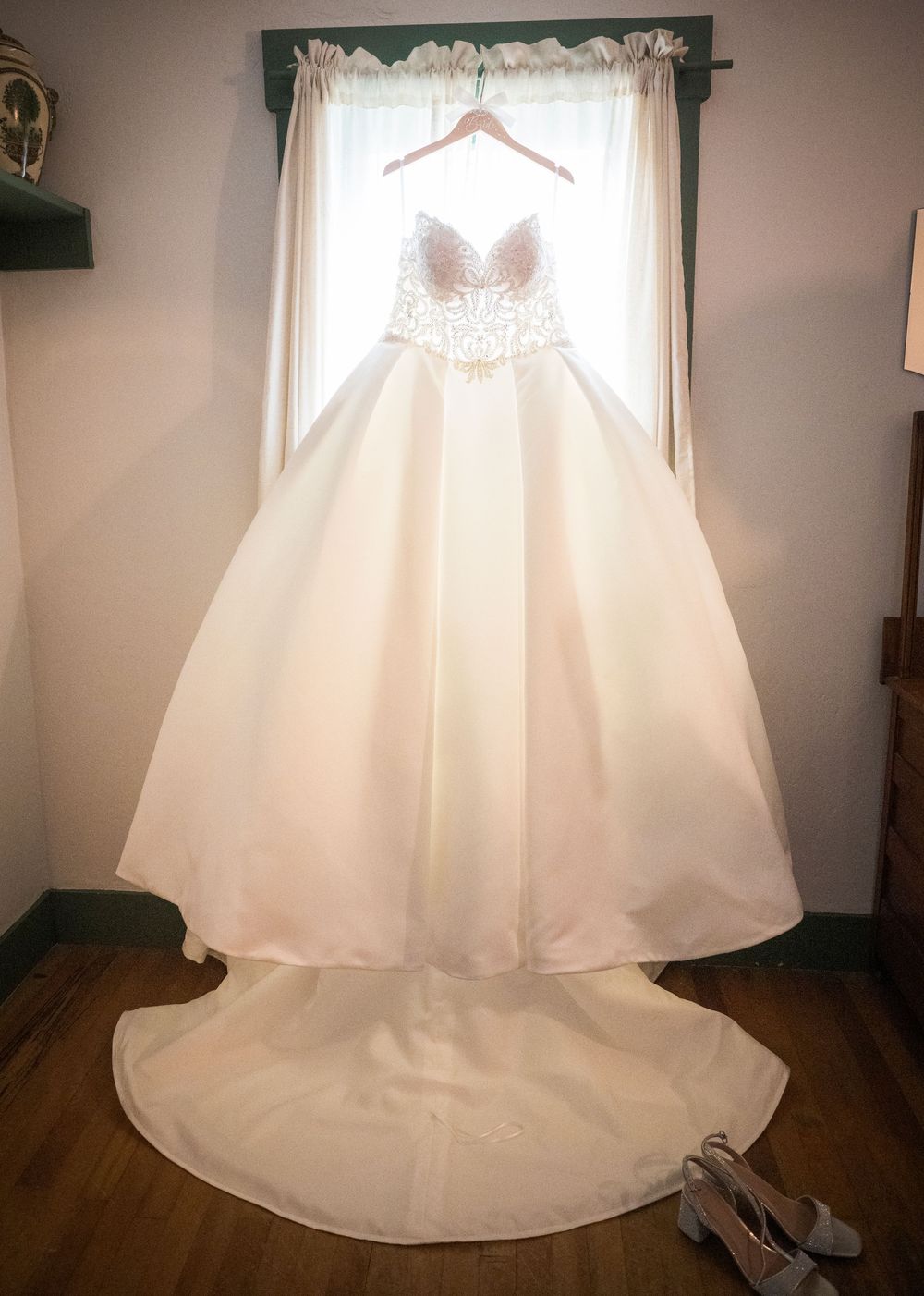 White wedding dress displayed on hangers in a room with natural window light.