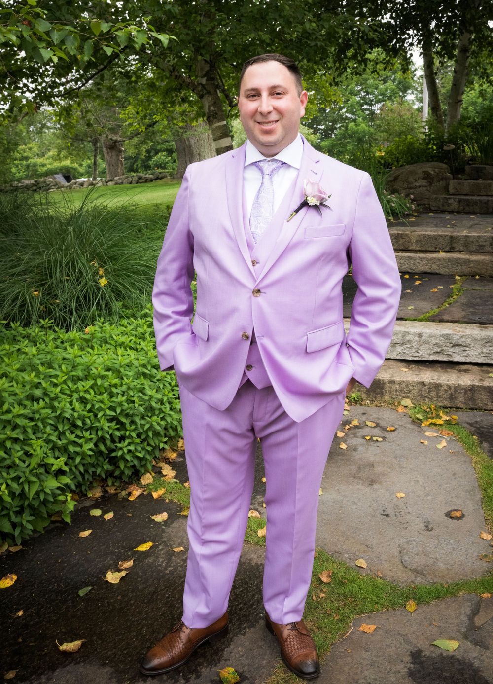 Lavender colored formal suit photographed in a garden setting with stone steps and greenery.