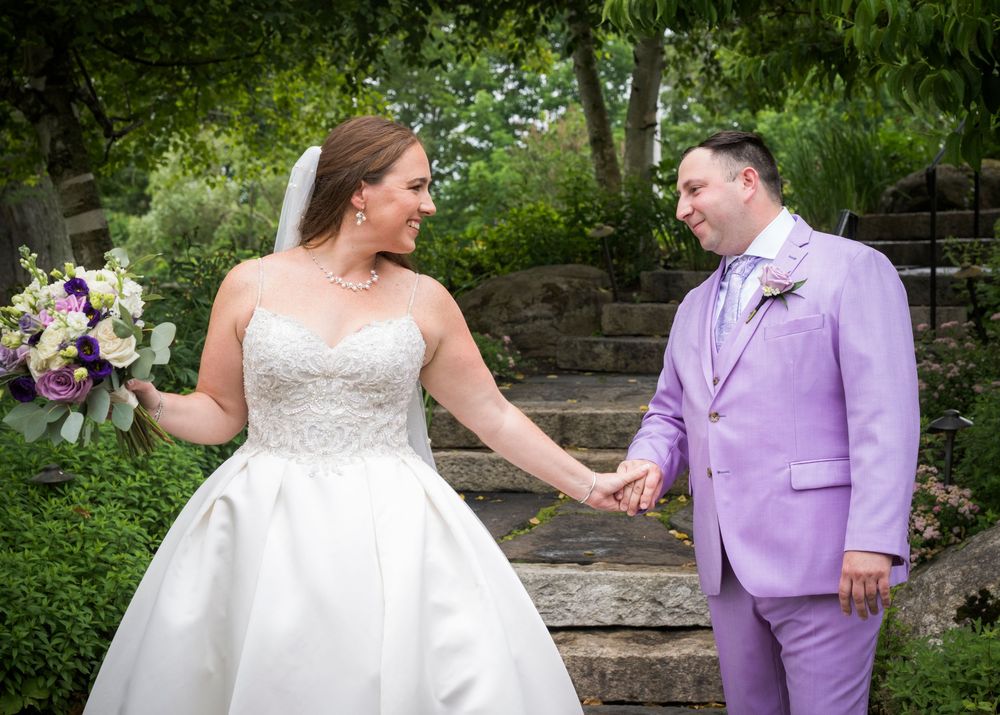 Wedding couple posing in a garden setting with lavender and white attire.