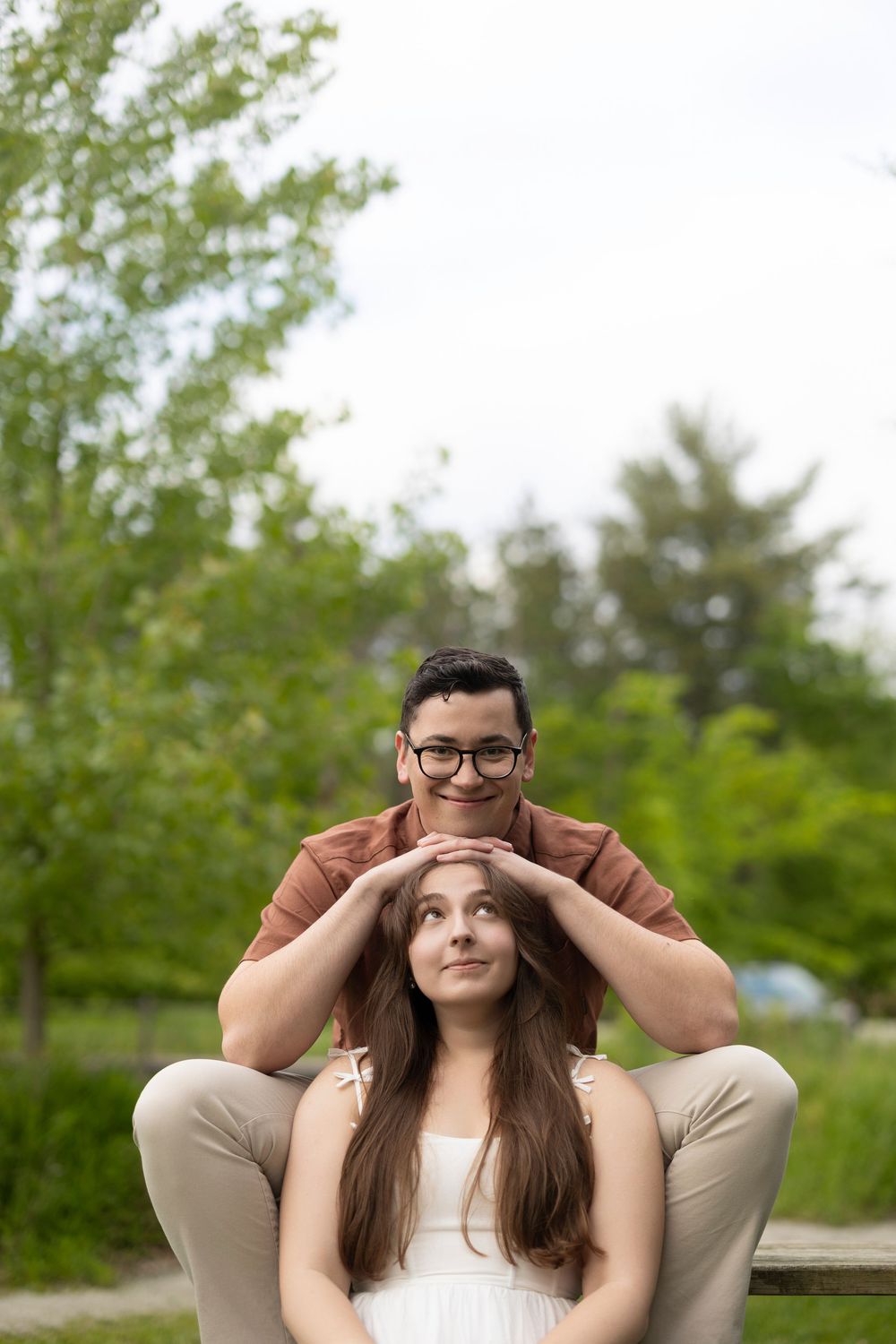 Playful couple posing together with partner placing hands on other's head in outdoor park setting.