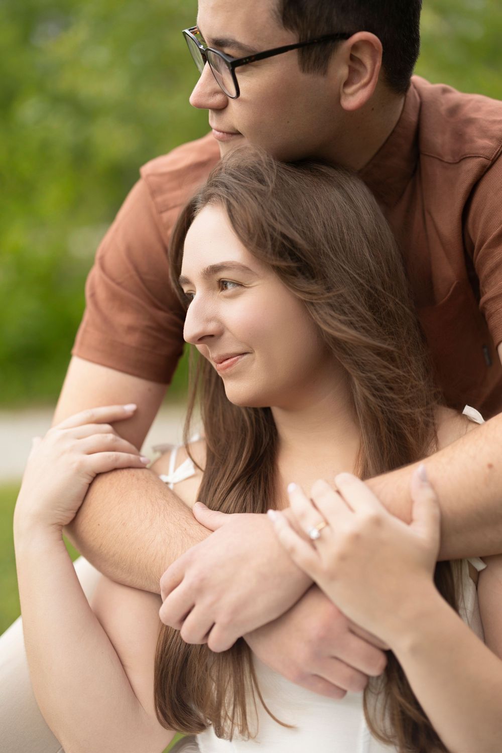 A romantic couple embraces outdoors in a tender moment against a green natural background.