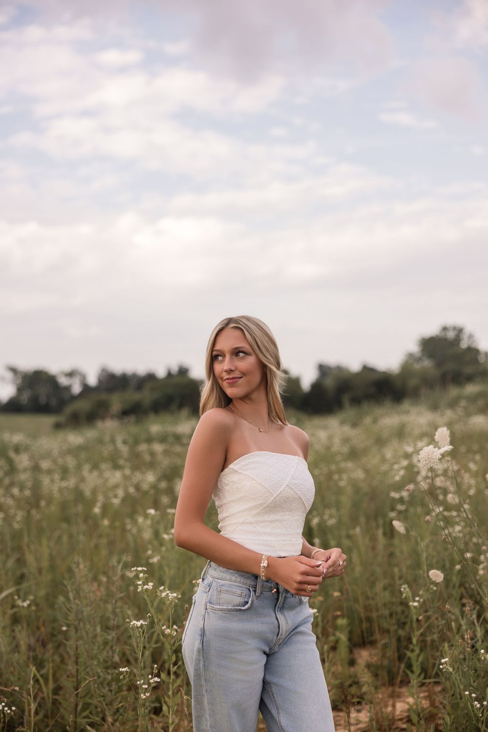 A summer portrait in a wildflower meadow featuring a white crop top and light wash jeans at sunset.