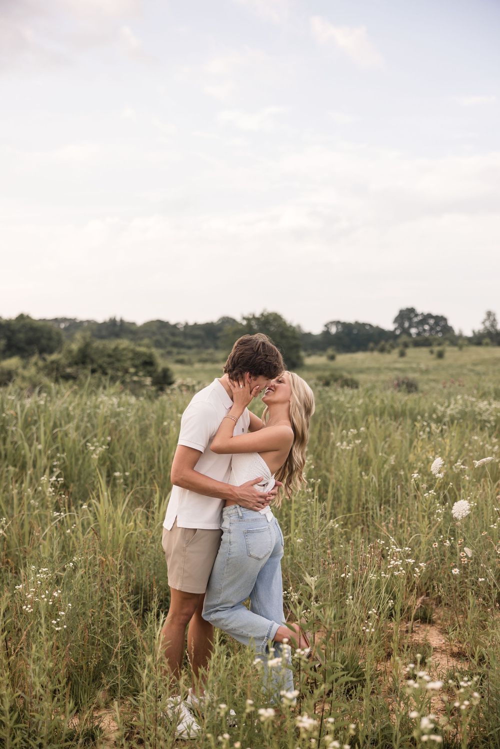 A romantic couple embraces in a serene meadow with wildflowers on a soft summer afternoon.
