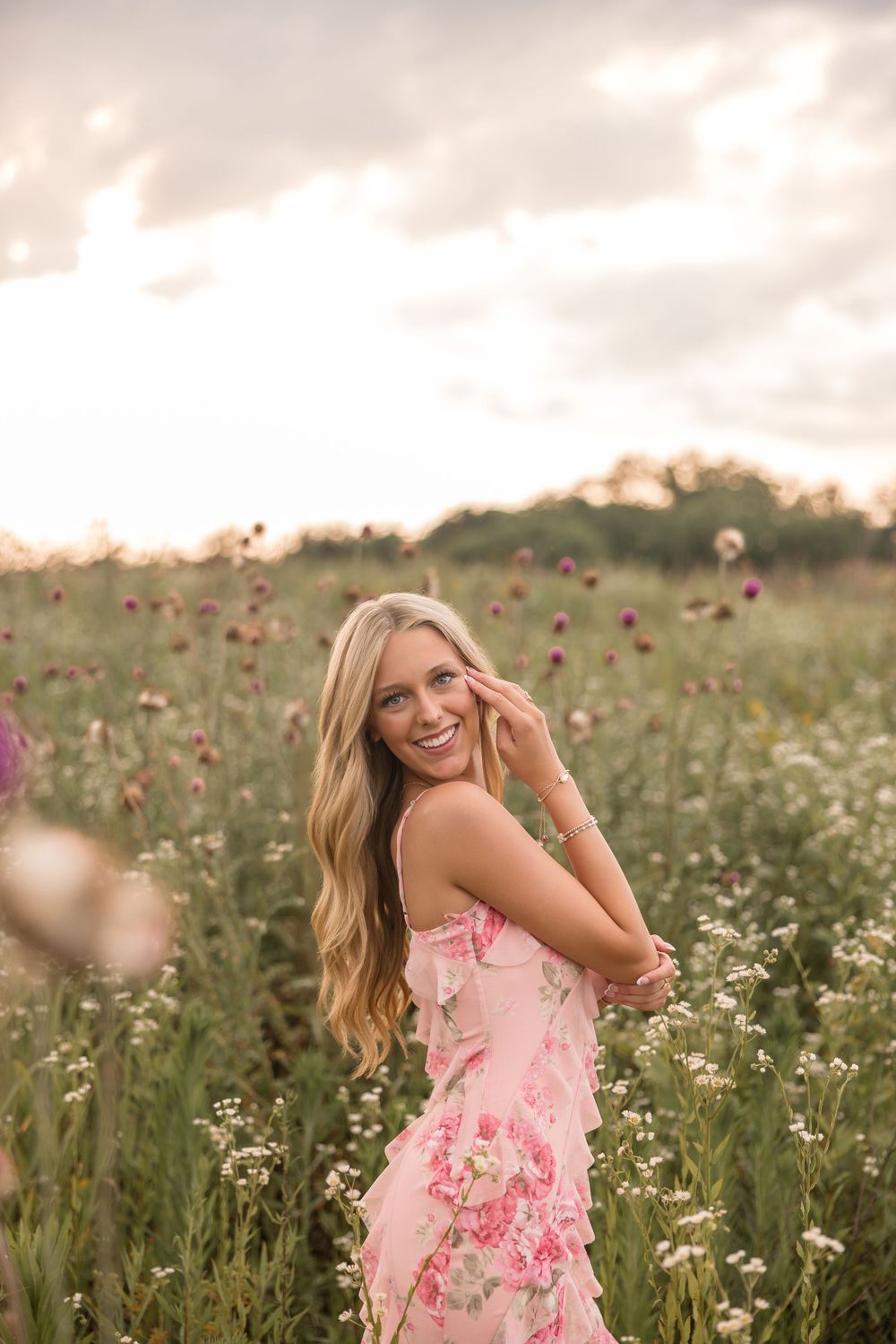 Woman in pink floral dress twirling playfully in a wildflower field at sunset.