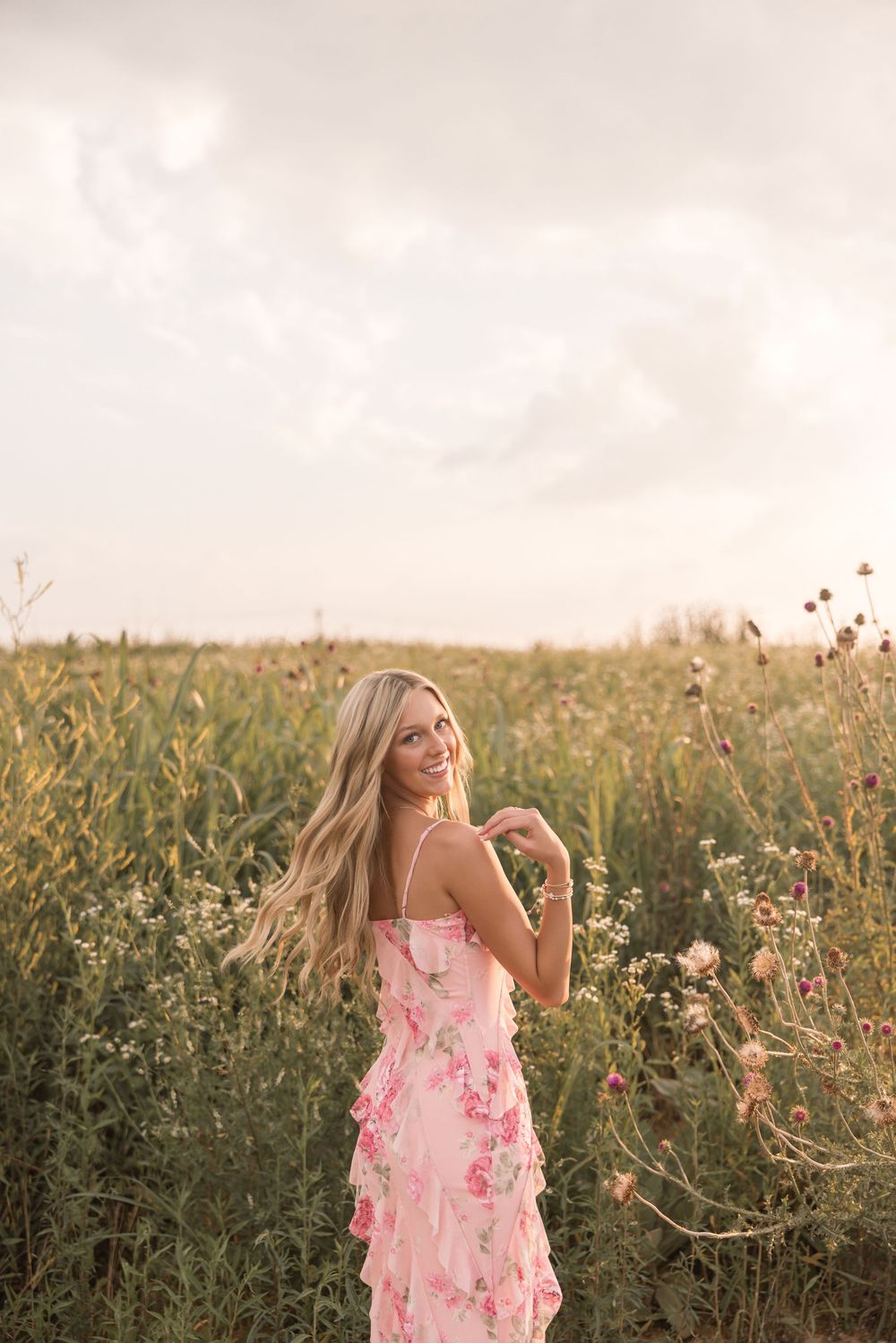 A person in a pink floral dress poses gracefully in a golden-hour lit wildflower field.