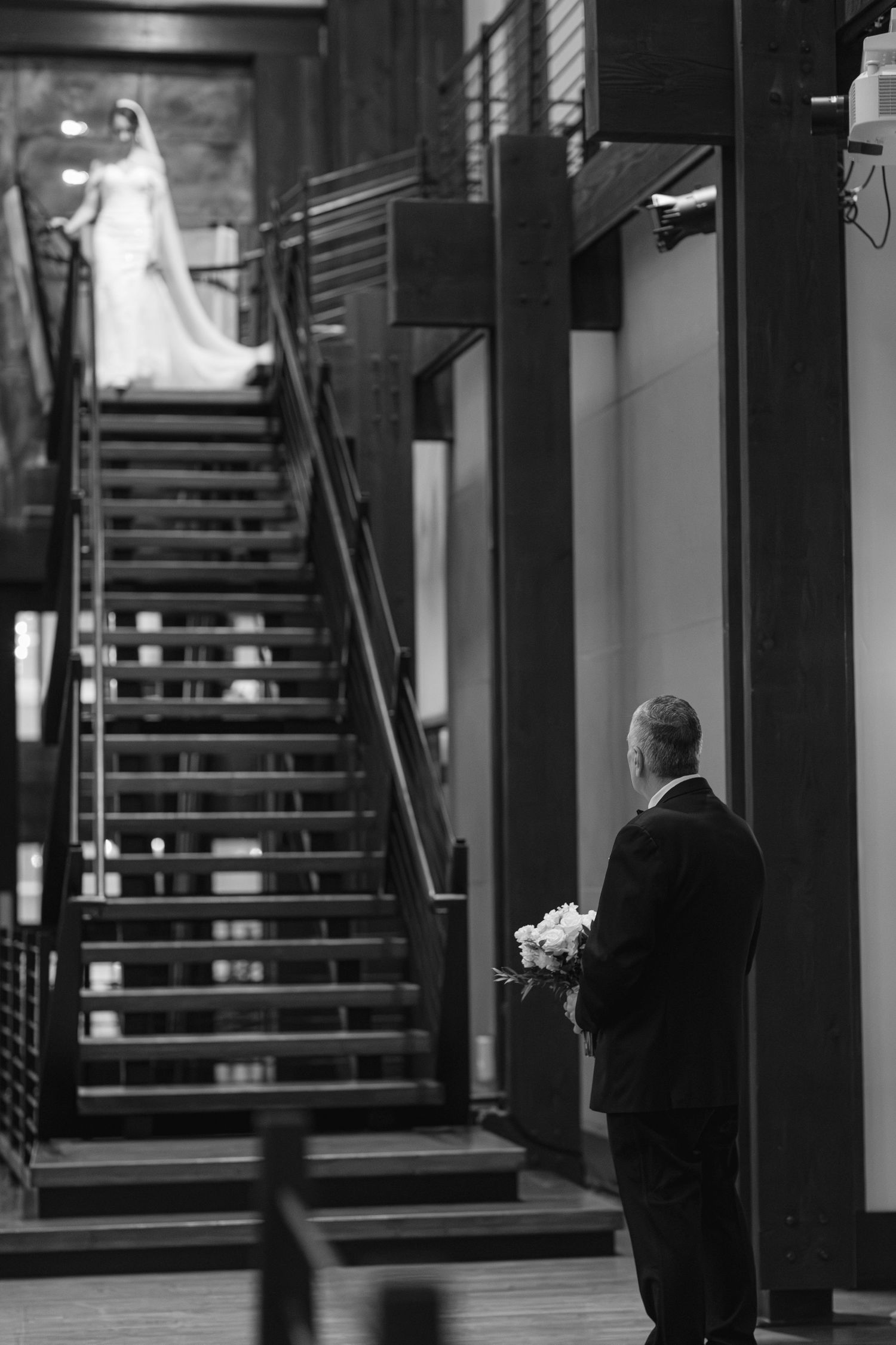 A person in a bridal gown stands at the top of a staircase while someone in a suit waits below with flowers. Top 10 Nashville Wedding Venues