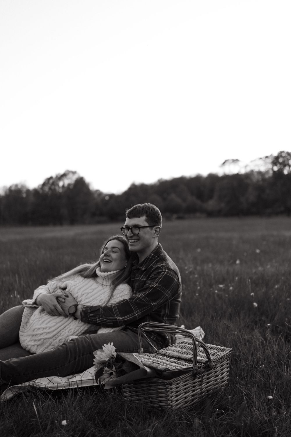 couple sitting on a blanket with picnic in open field hugging each other during outdoor maternity photoshoot in Stockholm