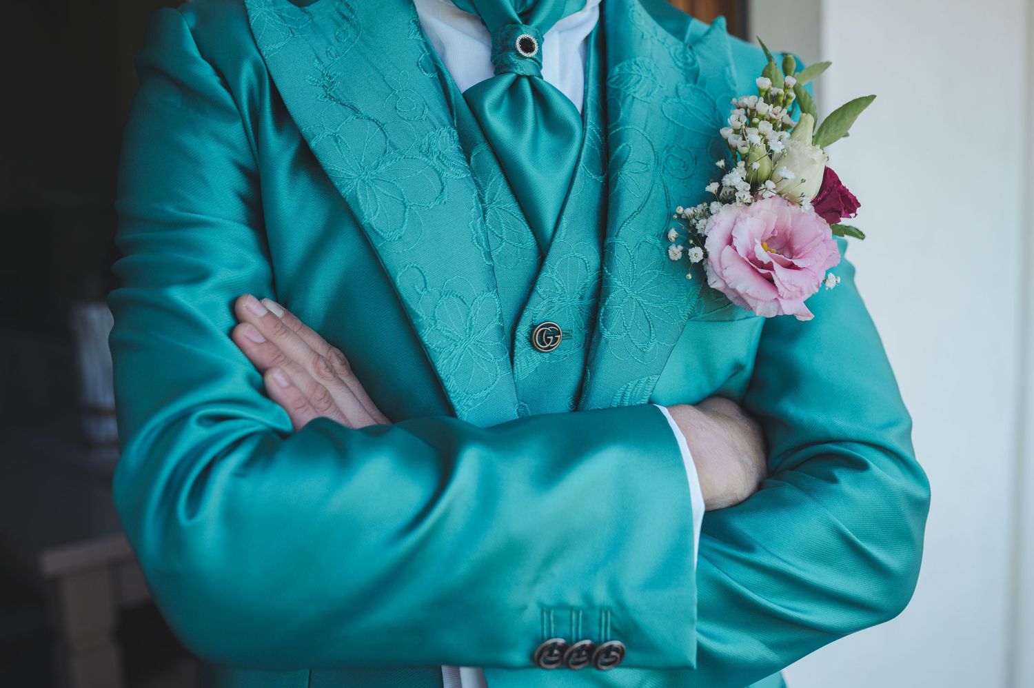 A turquoise suit jacket with pink floral boutonniere shown in detail.