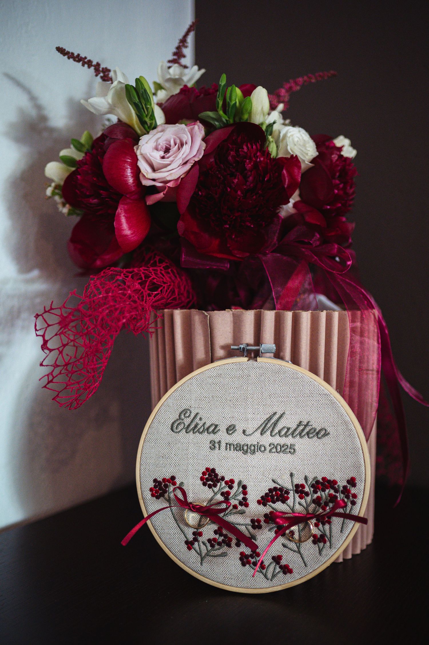 Wedding embroidery hoop with red and pink rose bouquet displays 'Elisa e Matteo' with burgundy floral design.