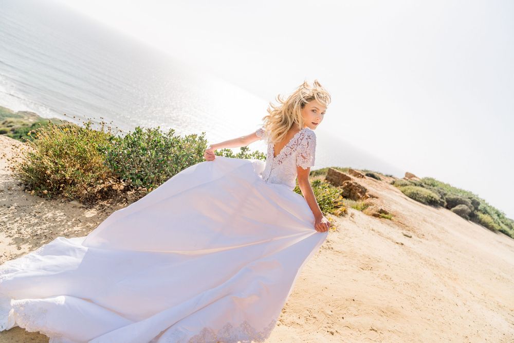 A flowing pink gown billows in the ocean breeze as someone stands on a coastal cliff during golden hour.