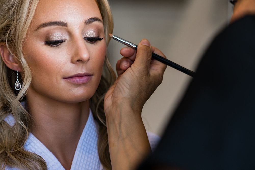 Professional makeup artist applying eyeshadow to bride during wedding preparation.