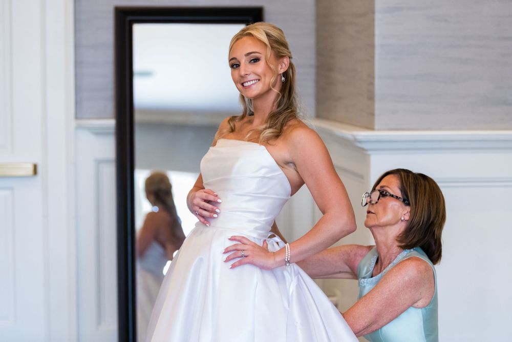 A bride in a white strapless wedding gown poses with her bridal party in a formal indoor setting.