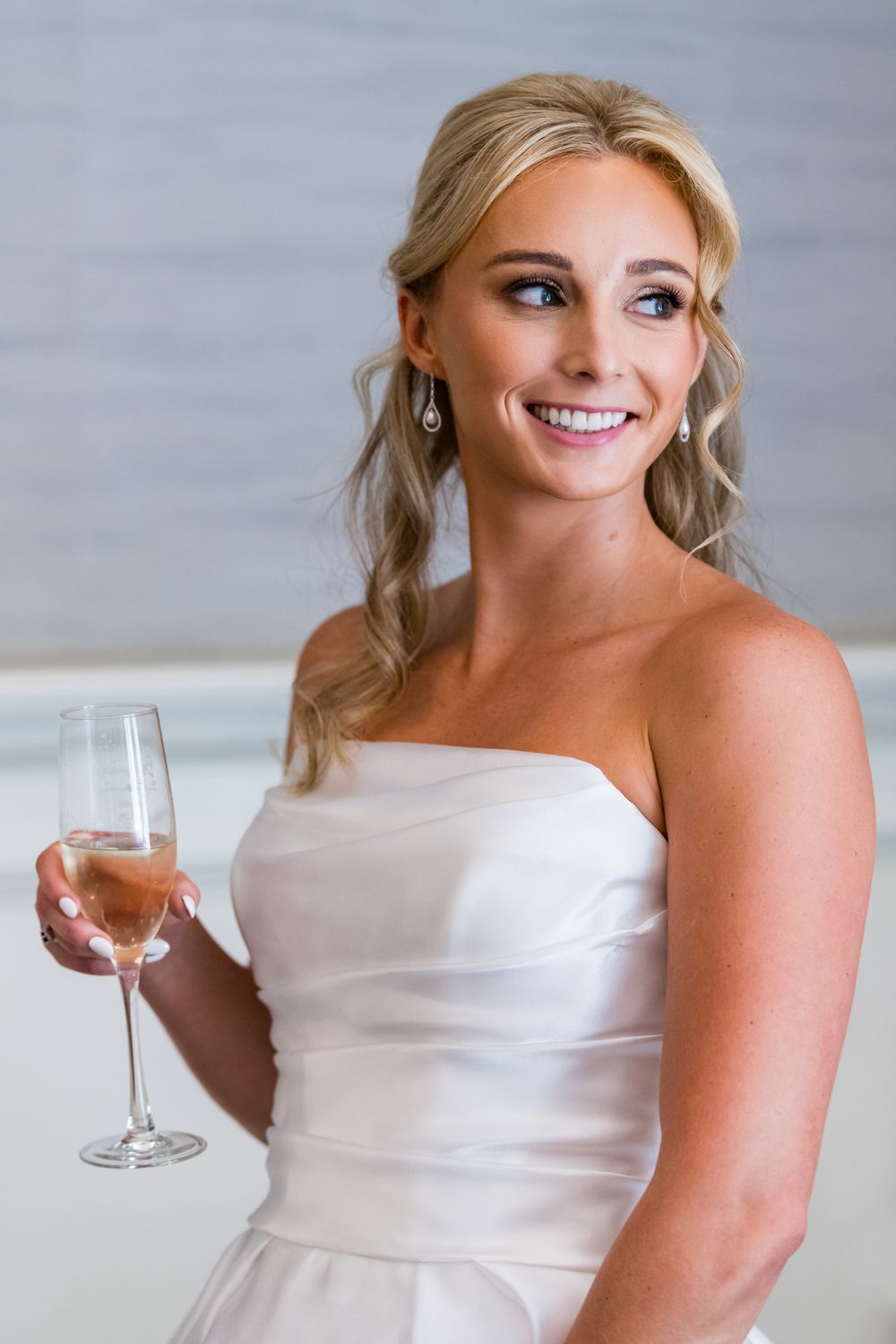 A person in a white strapless dress smiles while holding a wine glass against a gray background in multiple poses.
