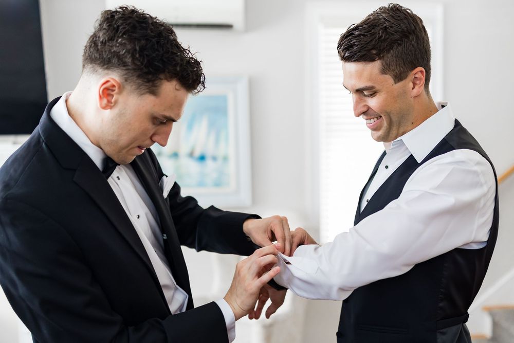 Two people in formal attire help each other with buttoning shirt cuffs while getting dressed for a special occasion.