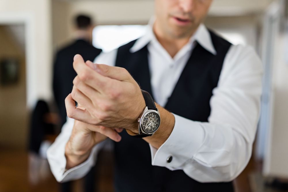 Close-up of groomsman adjusting watch and cufflinks while wearing formal attire.