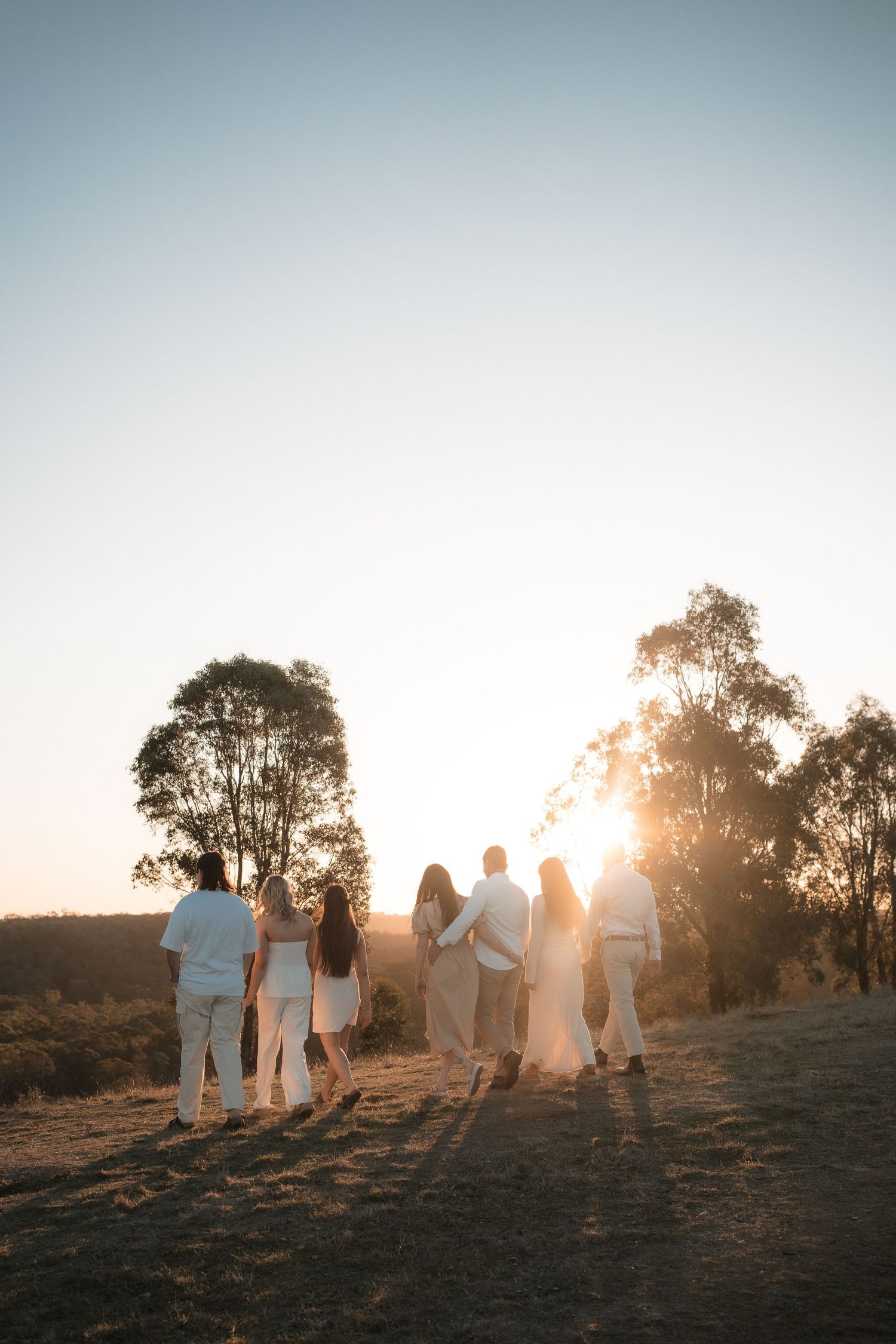A group of people walking together at sunset with eucalyptus trees silhouetted against a golden sky at Mt Lofty, Wonga Park