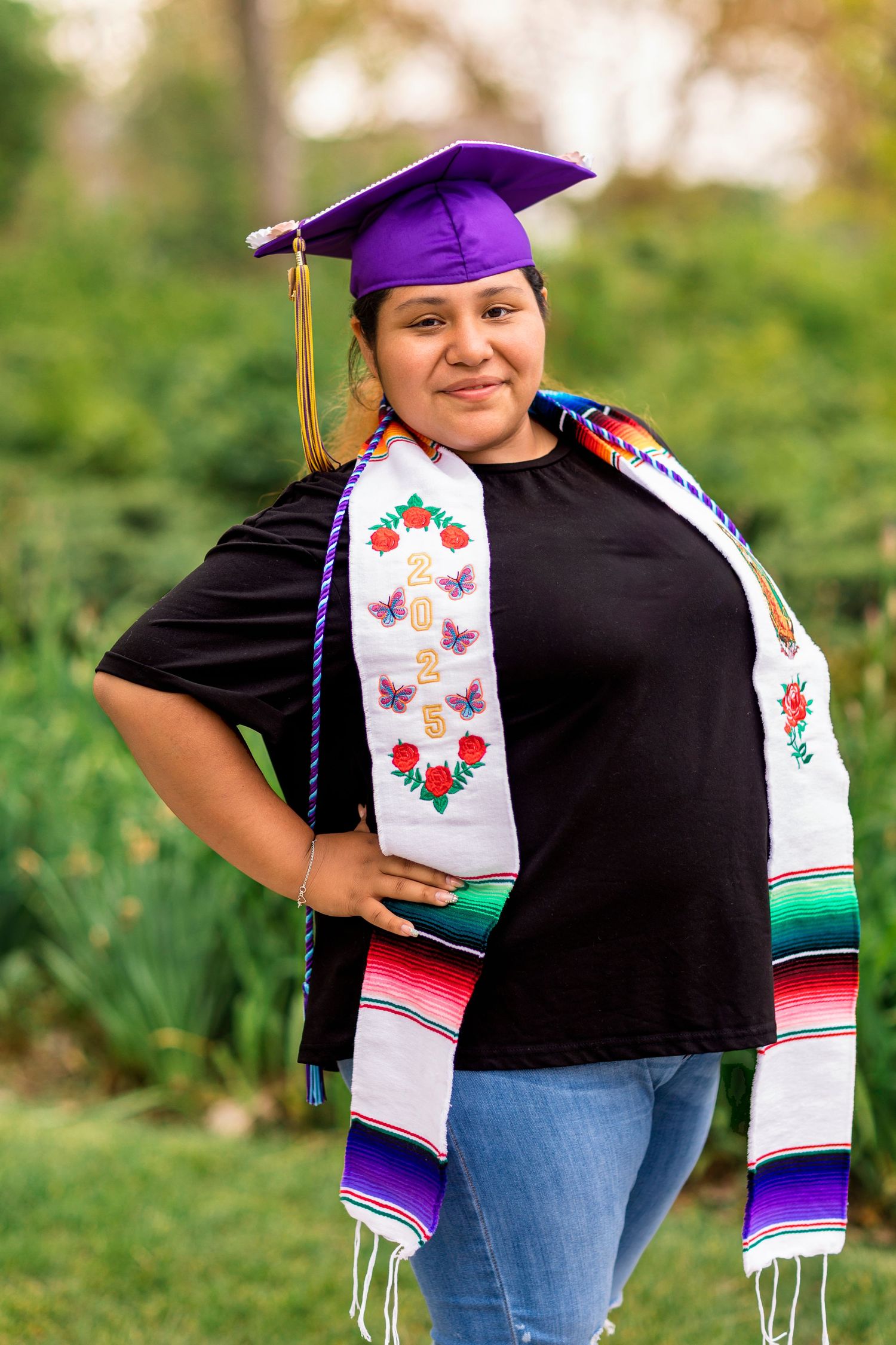 Alejandra stands in her cap and gown among dune grass at Van Buren Street Overlook in South Haven, Michigan, smiling softly