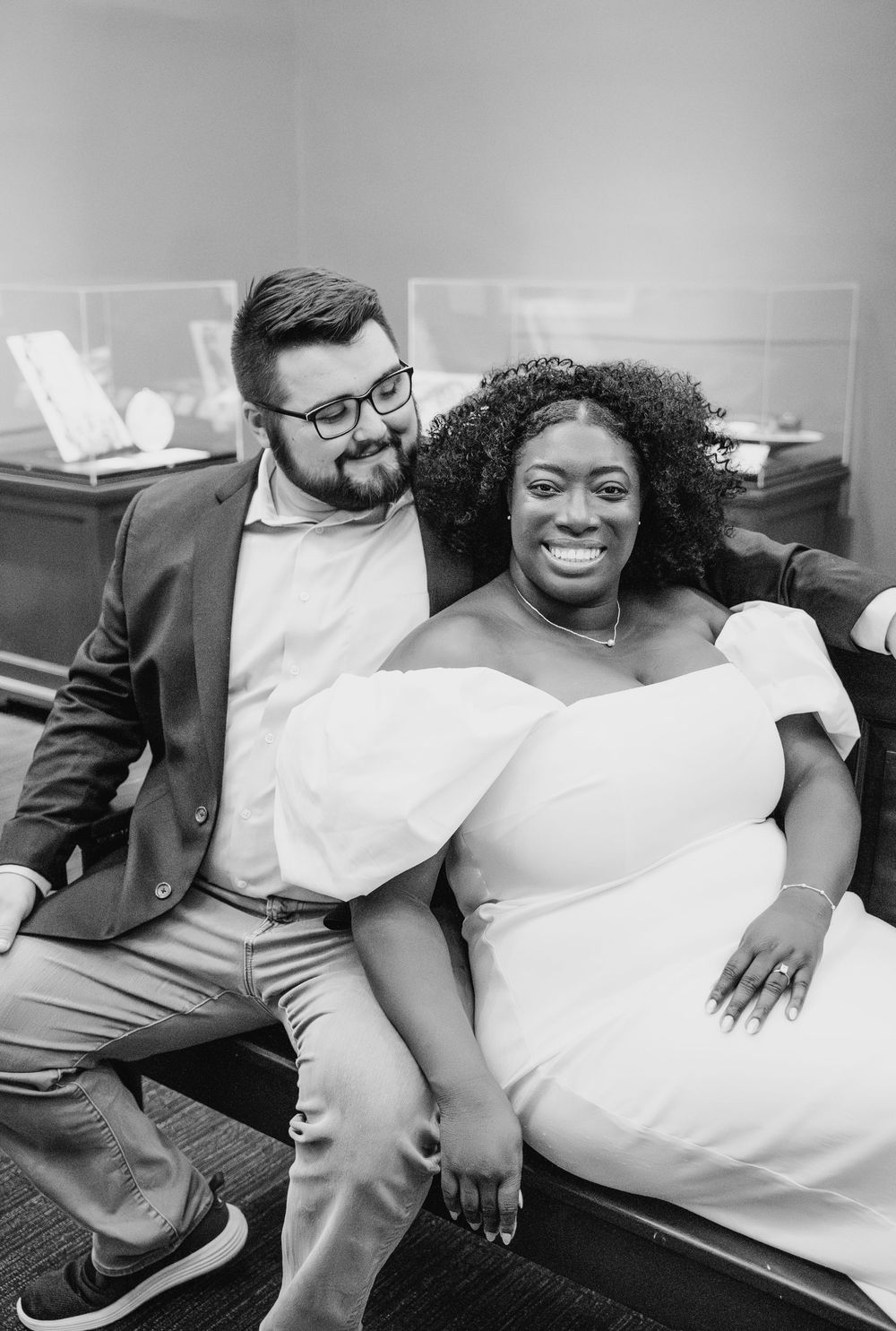 A candid black and white portrait of a couple sitting together on a sofa, sharing a joyful moment and genuine smiles.