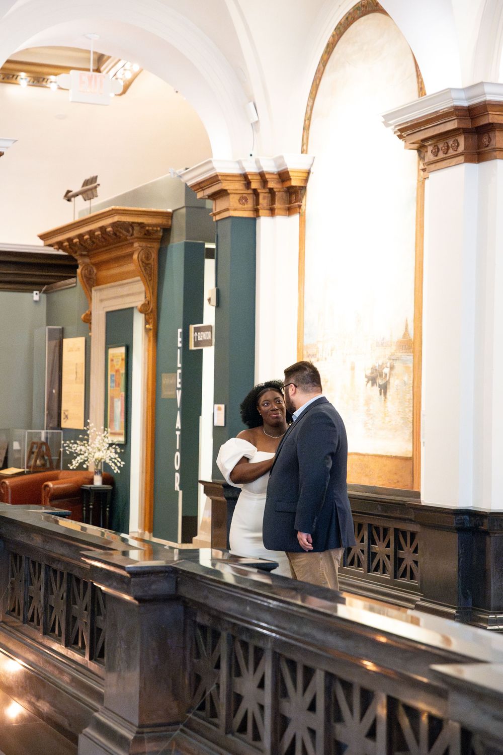 A couple shares an intimate moment in an elegant venue with ornate architectural details and arched columns.