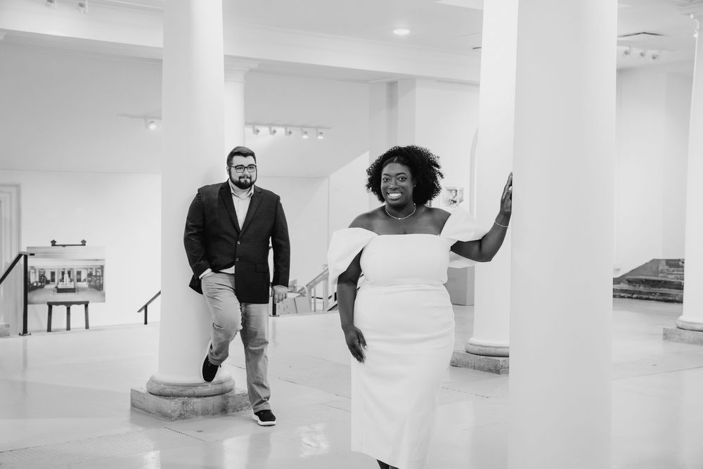 A joyful black and white photograph of a couple having fun in a bright modern interior with white columns.