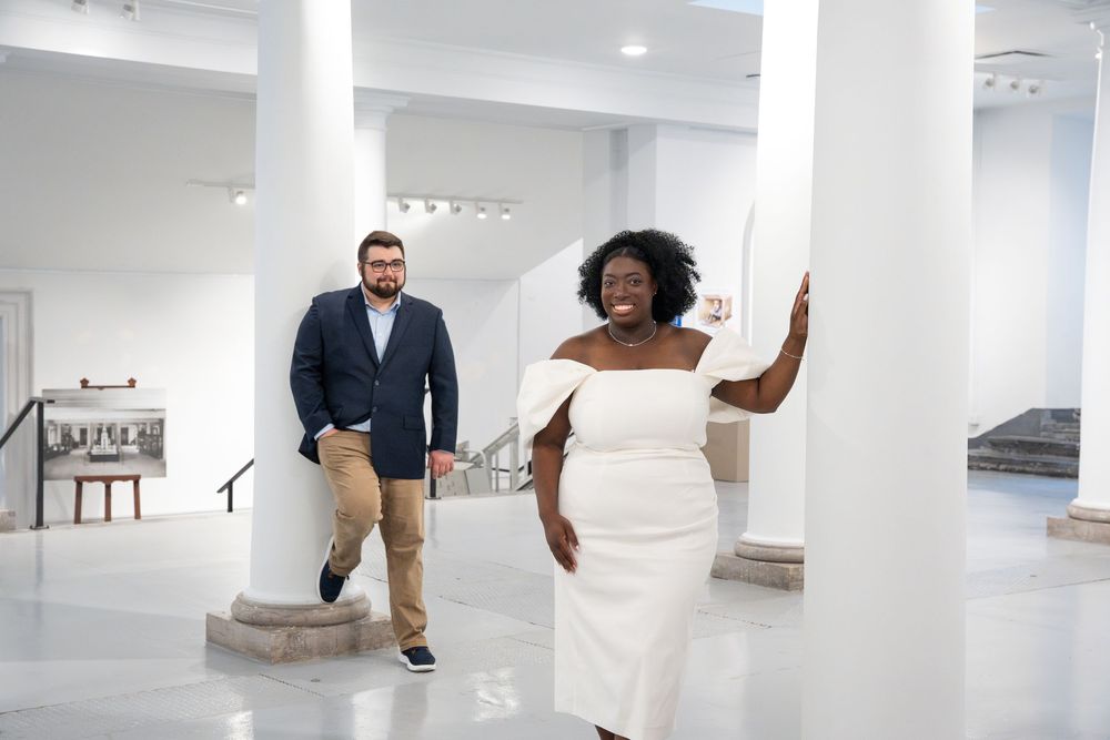 A couple enjoys a playful moment together in an elegant white modern space with columns.
