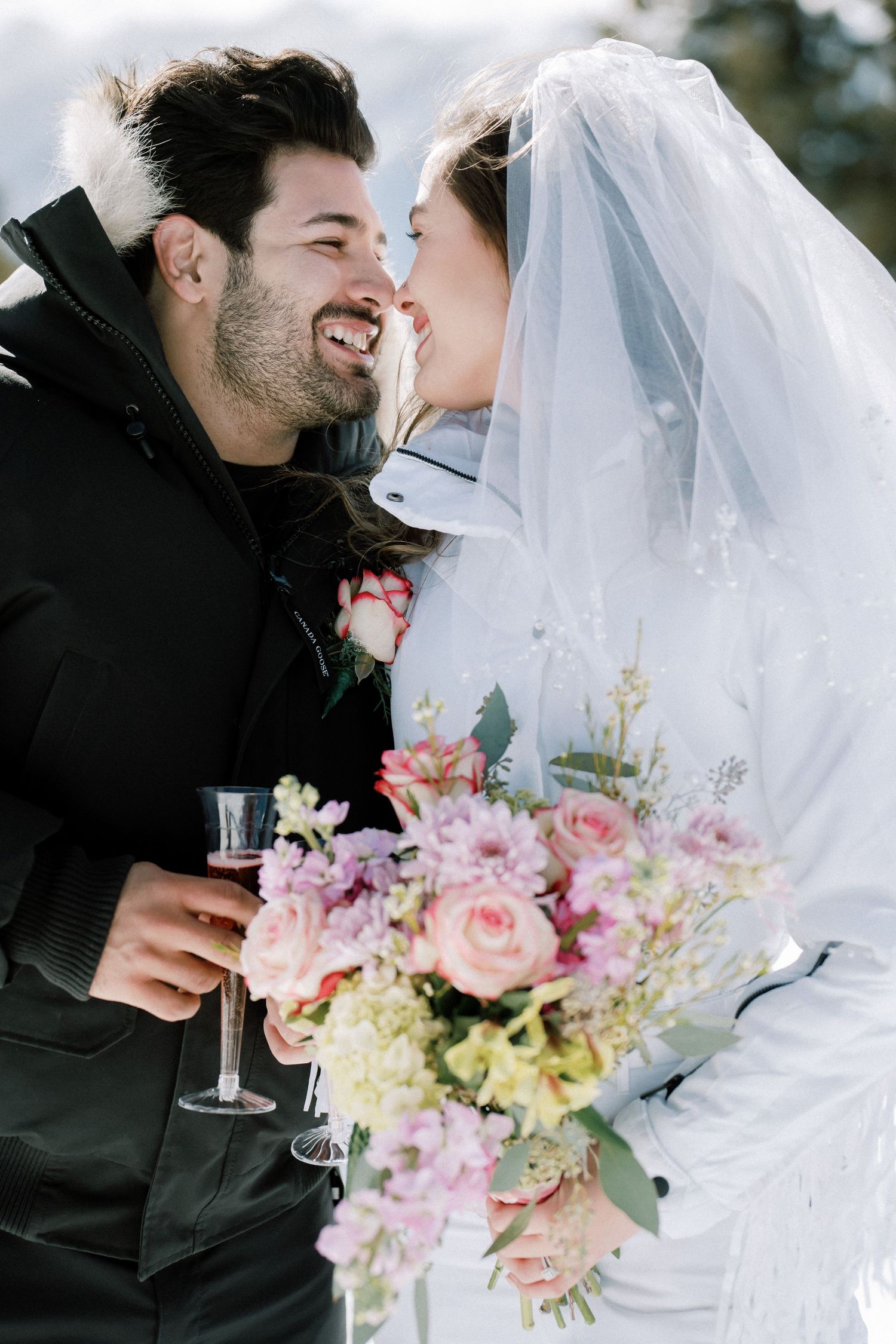 A joyful couple in a bridal portrait with the bride in white veil holding pink and cream floral bouquet.