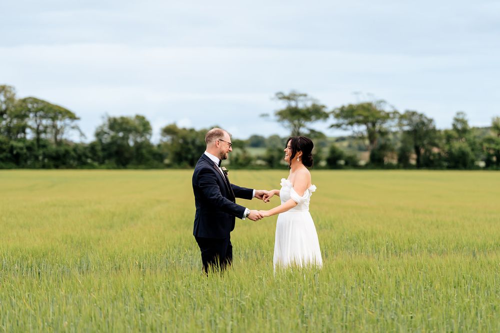 Wedding couple dances together in a sun-lit meadow filled with tall grass on their special day.