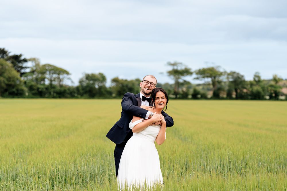 Couple shares joyful moment together in open green field during wedding photoshoot.
