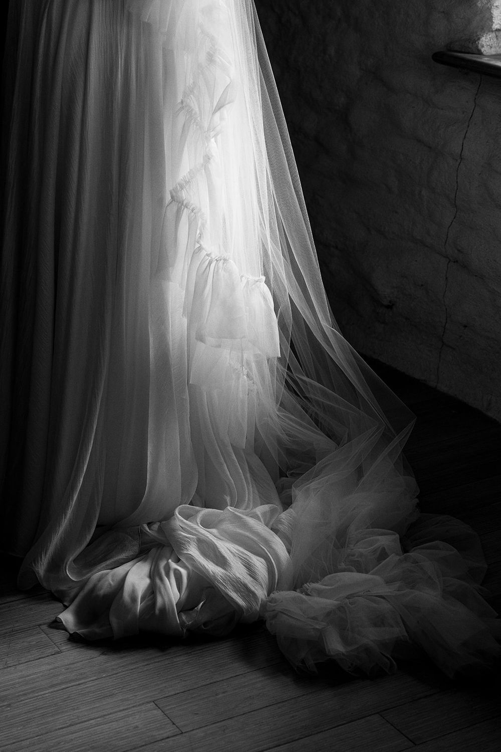 Dramatic black and white detail shot of flowing wedding dress train on wooden floor.