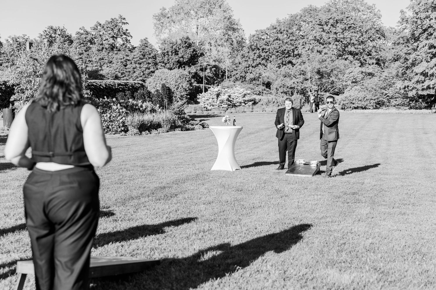 A black and white photograph shows people gathered on a grassy lawn during an outdoor event on a sunny day.