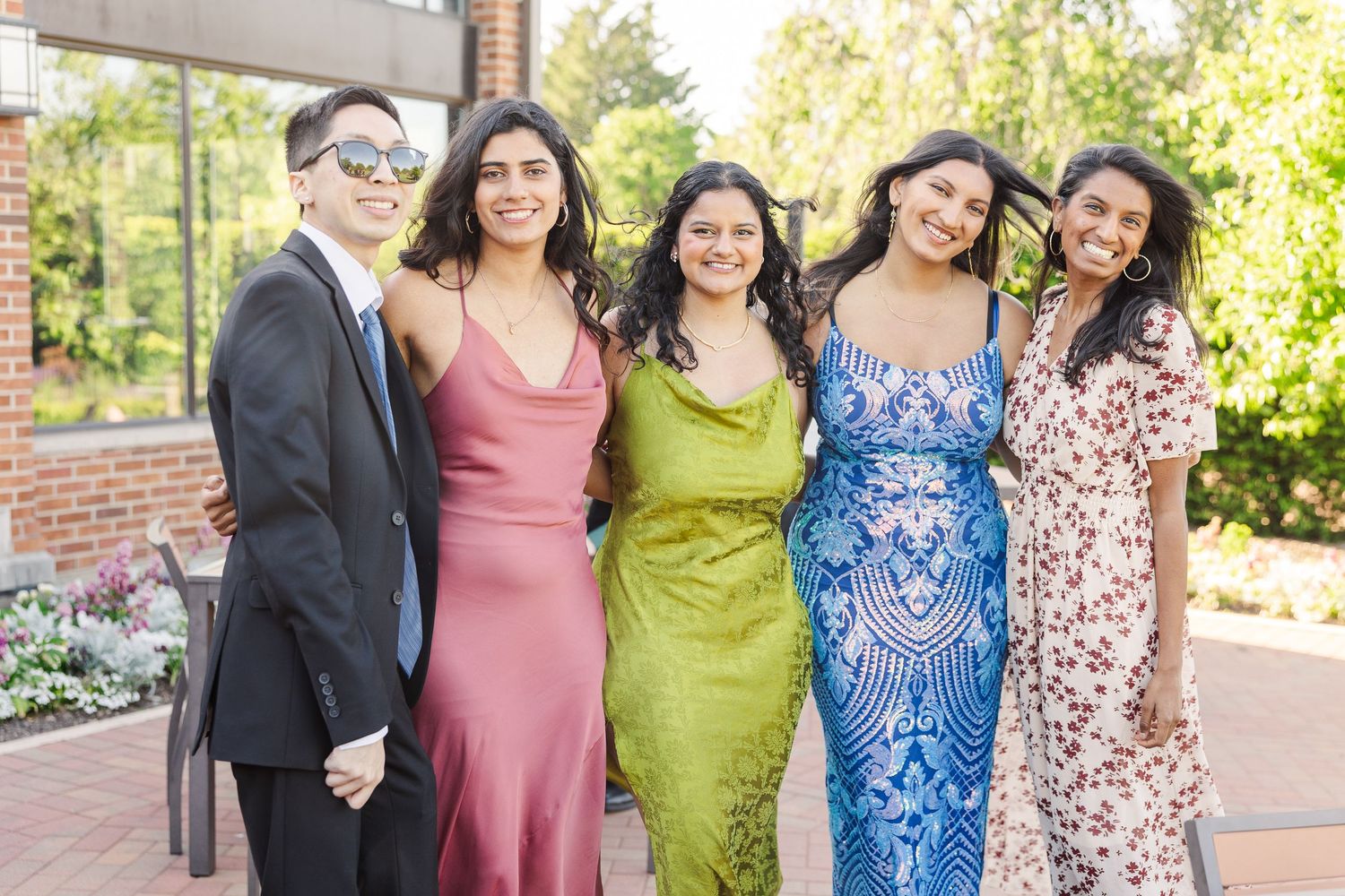 Group posing together outdoors in formal attire including pink, green, blue and floral dresses and dark suit.