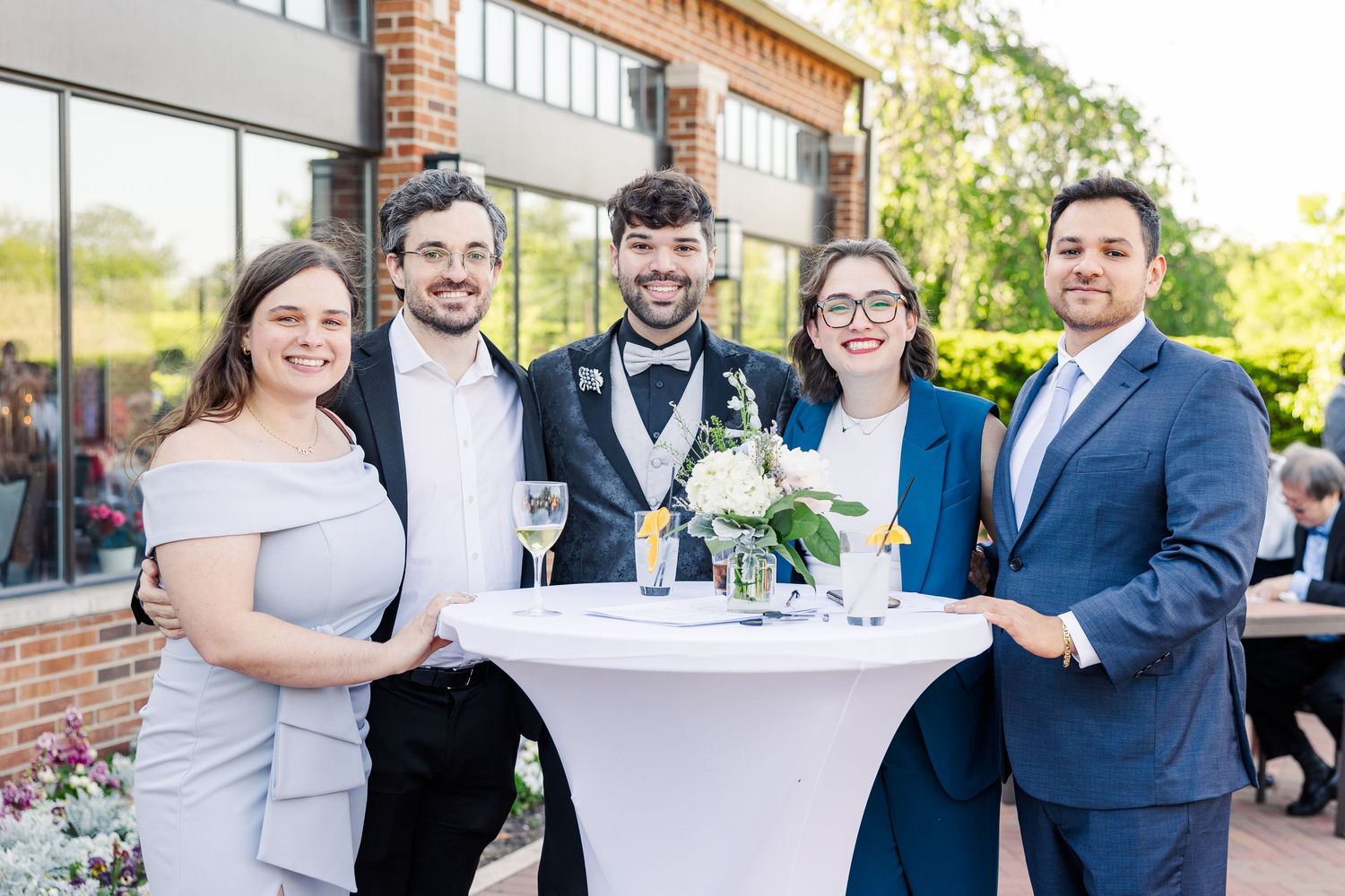 A group stands together around a cocktail table on an outdoor patio during a formal event.