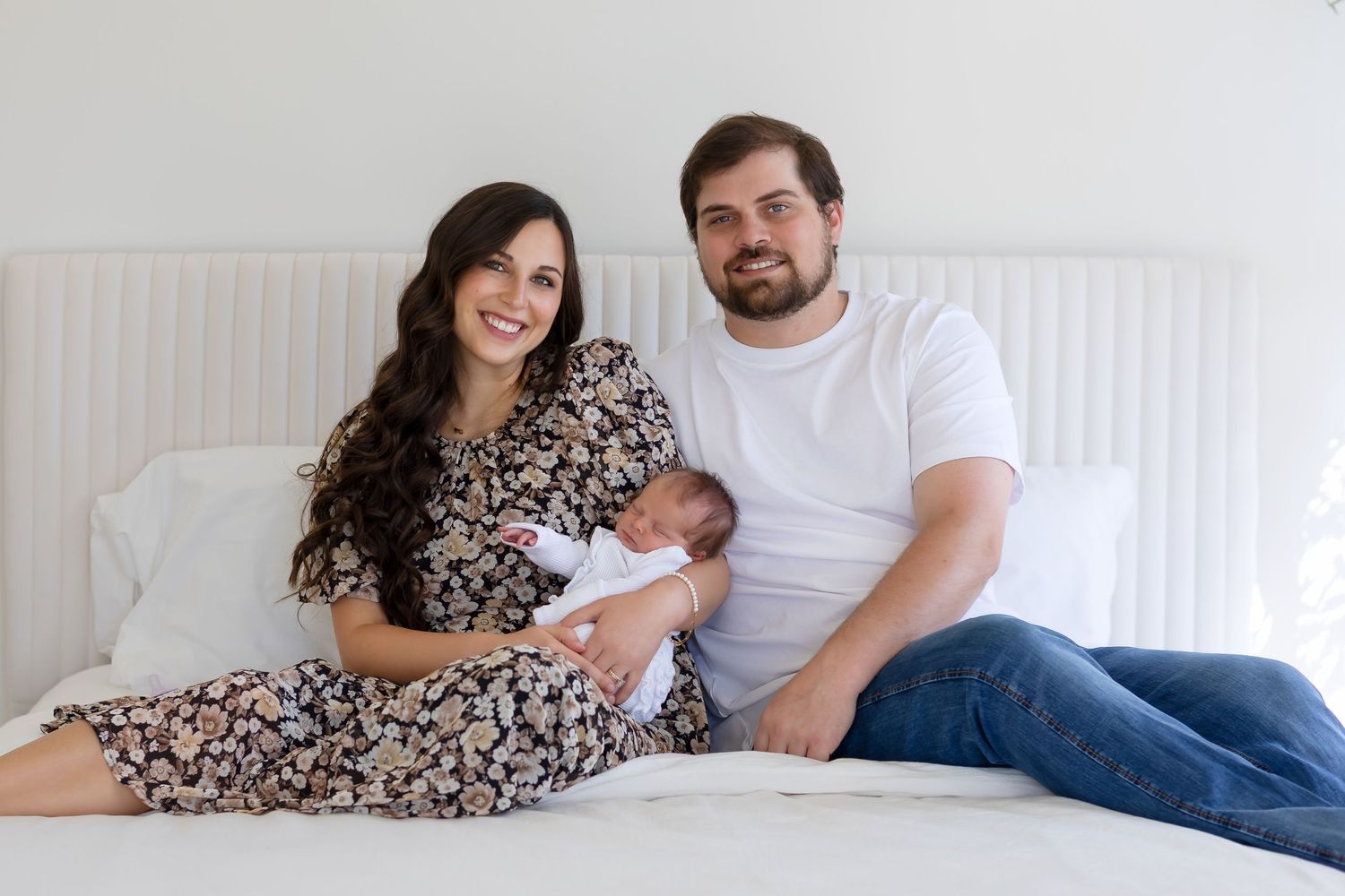 Couple holds new baby girl on white bed during in-home newborn photography session in Athens, GA.