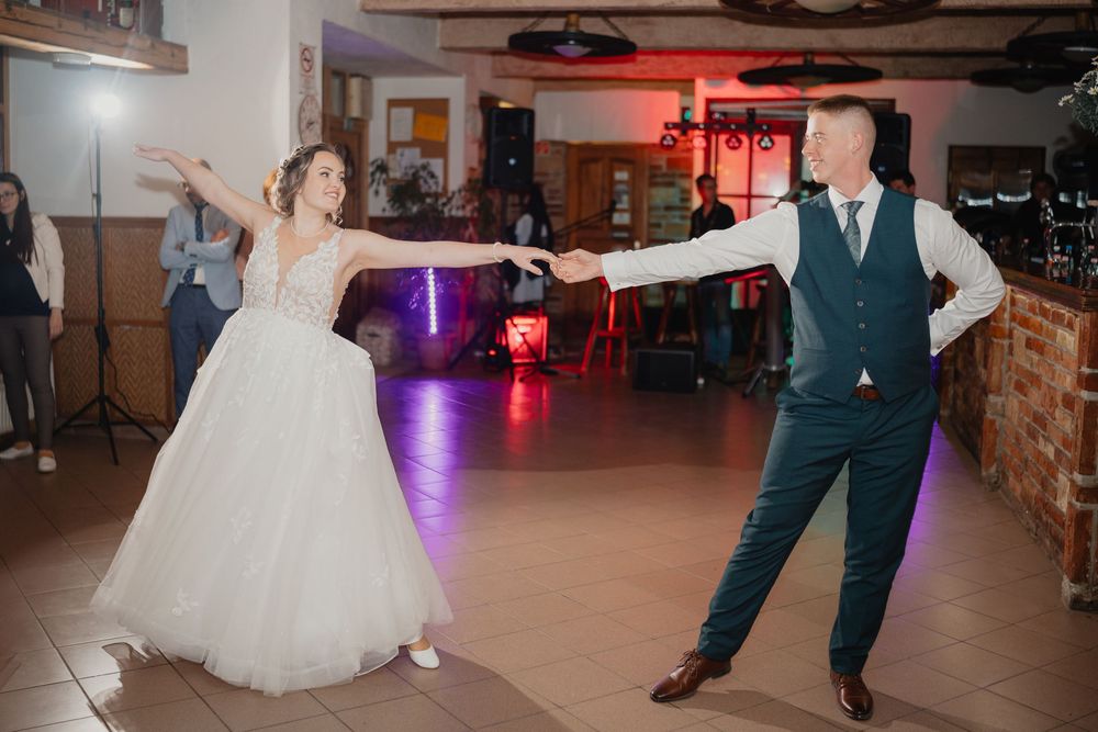 A couple dances together on their wedding day at a reception venue with purple mood lighting and rustic decor.