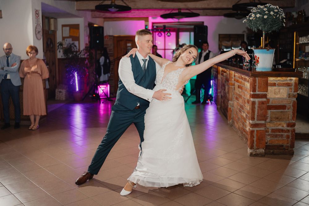 A couple performs their first dance at their wedding reception in a venue with purple lighting and a rustic bar.