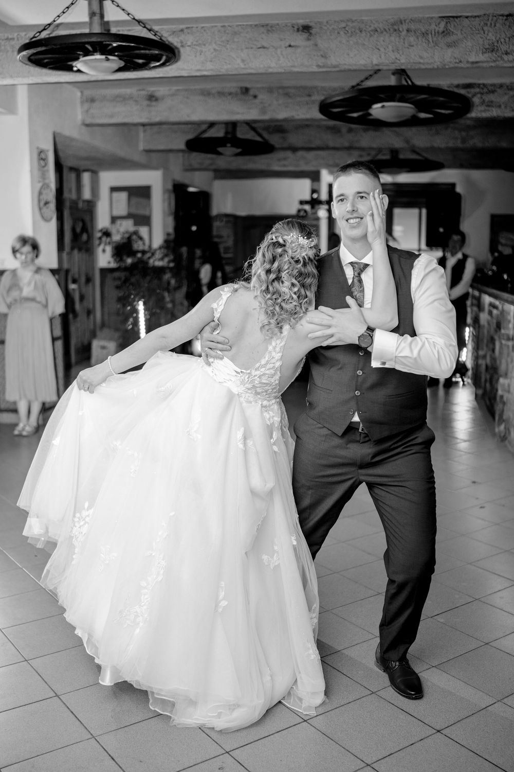 A black and white photo of a couple dancing at a wedding reception with circular pendant lights overhead.