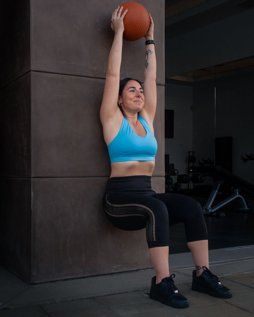A person in athletic wear performs a wall sit while holding a medicine ball overhead. Brand photography, San Diego, California