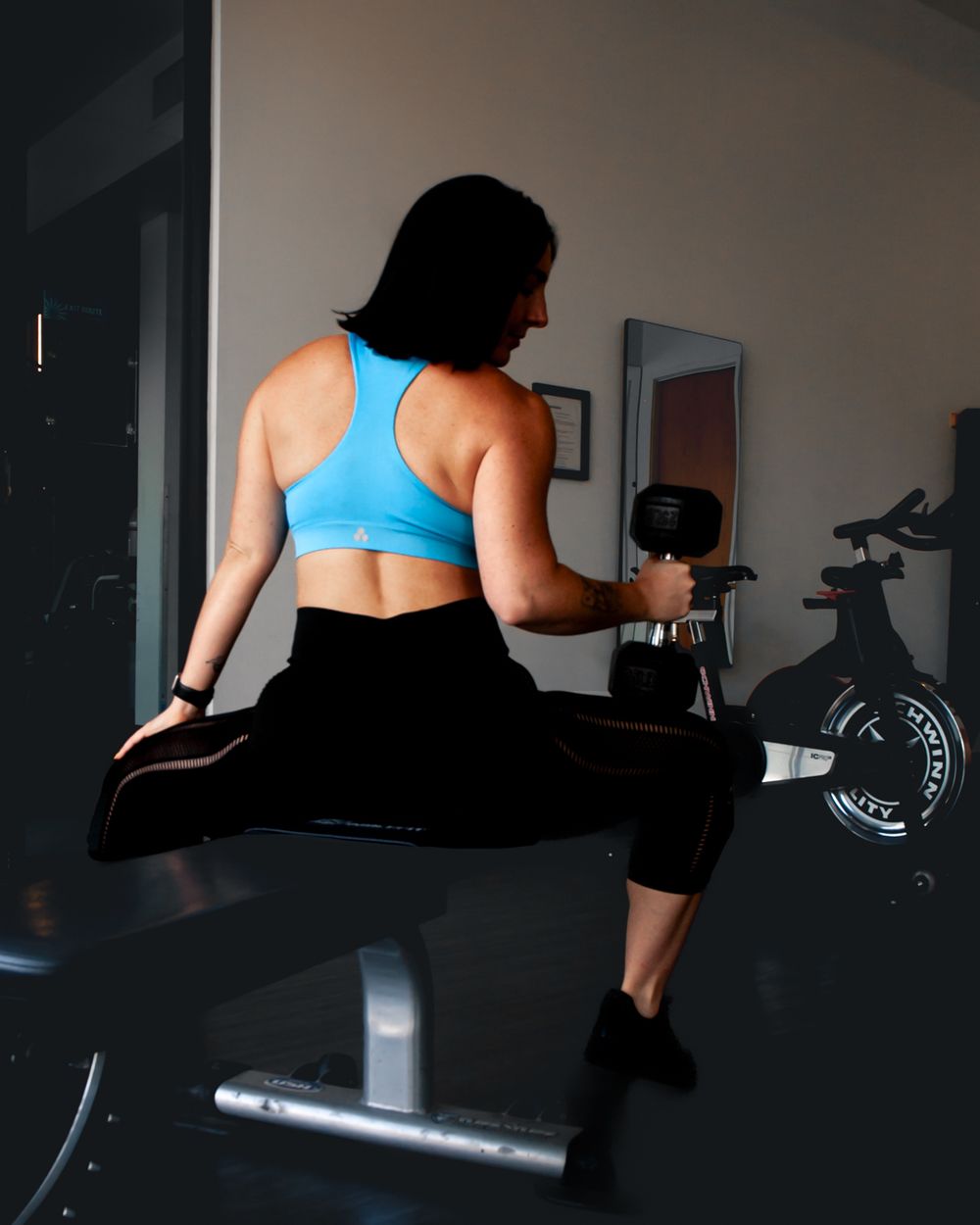 A person in blue workout top performs stretches on exercise equipment in a gym setting. Brand photography, San Diego, California