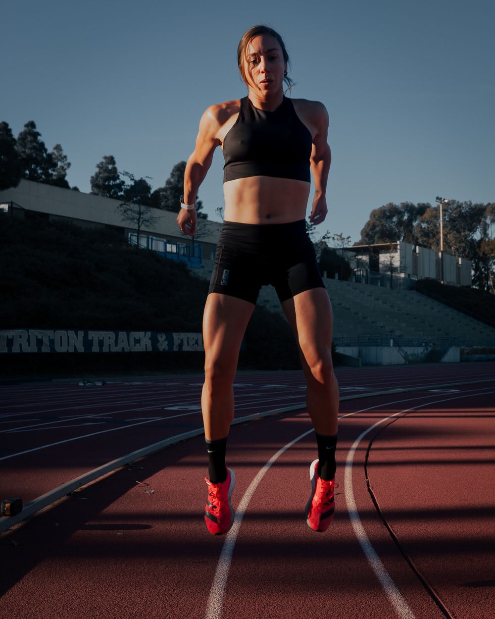 An athlete in black workout gear does a jump exercise on an outdoor running track. Brand photography, San Diego, California