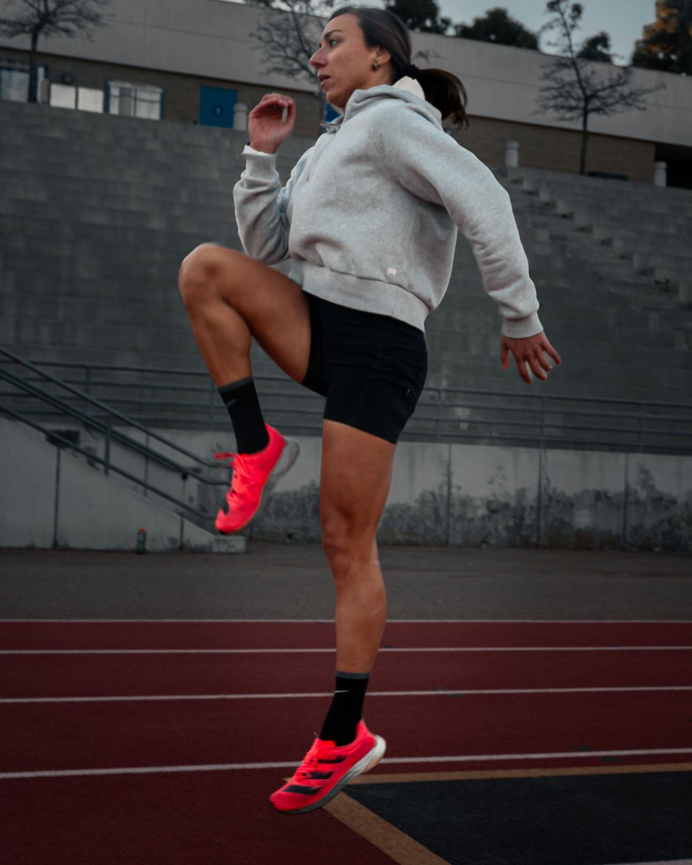 Athletic person jumping on a running track wearing bright pink sneakers and a gray hoodie. Brand photography, San Diego, California