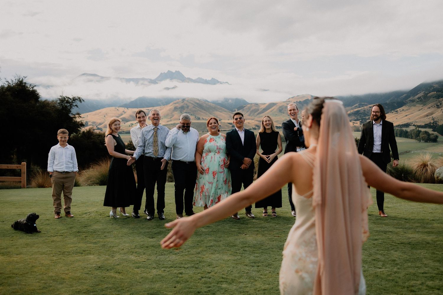 Wedding celebration on a grassy hilltop overlooking scenic mountain landscape during overcast weather.