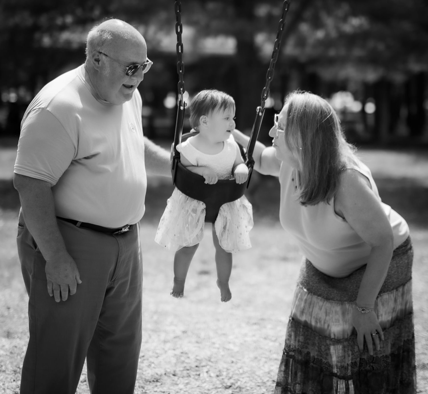 Black and white photo of family members at a playground with a small child on a swing.