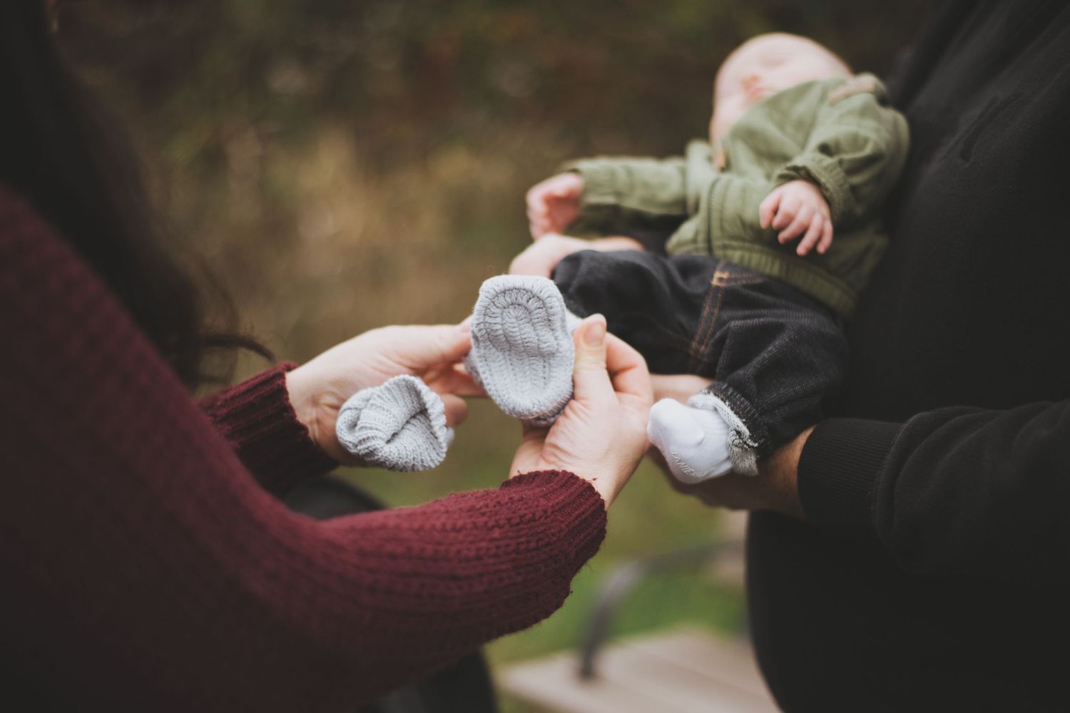 Close up view of hands holding tiny white baby socks outdoors in a natural setting.